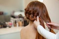 Beautiful, red-haired girl with long hair, hairdresser weaves a French braid, in a beauty salon. Royalty Free Stock Photo