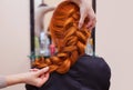 Beautiful, red-haired girl with long hair, hairdresser weaves a French braid, in a beauty salon Royalty Free Stock Photo