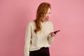 A beautiful red-haired girl with red lipstick stands on a pink background and screams at the phone in her hand Royalty Free Stock Photo