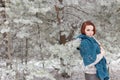 Beautiful red-haired girl with a scarf on his shoulders walking in the winter forest of firs and pines stilled Royalty Free Stock Photo