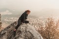 Red-haired girl is sitting on the stones above the precipice against the backdrop of mountains and fog Royalty Free Stock Photo