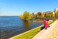 Girl in a red hood uses a mobile phone while sitting on the river bank