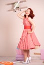 Beautiful red-haired pinup smiling happily girl posing in a retro red dress and white high heels Royalty Free Stock Photo