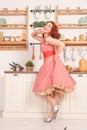 Beautiful red-haired pinup smiling happily girl posing in a retro red dress and white high heels Royalty Free Stock Photo