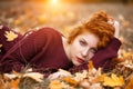 Beautiful red haired woman in autumn park lies in fallen foliage on a Sunny day, the light