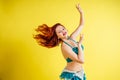 Beautiful red-haired woman dancing oriental belly dance in blue suit on yellow background in studio