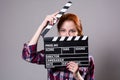 Beautiful red-haired woman holding a movie clapper, isolated over gray background Royalty Free Stock Photo