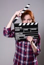 Beautiful red-haired woman holding a movie clapper, isolated over gray background. Royalty Free Stock Photo
