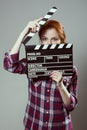 Beautiful red-haired woman holding a movie clapper, isolated over gray background. Royalty Free Stock Photo