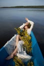 Beautiful red-haired woman lies in boat with flowers in her hands. Beauty romantic portrait girl in long white dress in wooden Royalty Free Stock Photo