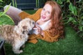 Beautiful red-haired woman plays with her dog in the garden