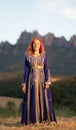 Beautiful red-haired woman in a traditional blue dress with goldwork ornamentations in a sunny field