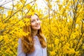 Beautiful red-haired young woman standing near blooming Forsythia bushes in spring garden