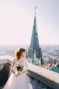 Beautiful red-head bride posing with bouquet on old castle balcony, cityscape background Royalty Free Stock Photo