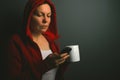 Beautiful red hooded woman drinking coffee and sending text mess