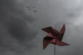 A red pinwheel against a dramatic sky with dark clouds and a flock of birds flying high in the sky Royalty Free Stock Photo