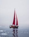 Beautiful red sailboat in the arctic next to a massive iceberg showing the scale. Cruising among floating icebergs in