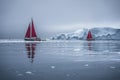 Beautiful red sailboat in the arctic next to a massive iceberg showing the scale. Cruising among floating icebergs in