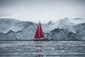 Beautiful red sailboat in the arctic next to a massive iceberg showing the scale. Cruising among floating icebergs in