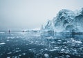 Beautiful red sailboat in the arctic next to a massive iceberg showing the scale. Cruising among floating icebergs in