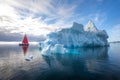 Beautiful red sailboat next to a massive iceberg. Royalty Free Stock Photo