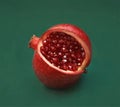 Beautiful red sliced pomegranate on a green background. Pomegranate fruit with red shiny beads, garnet crystals instead of seeds