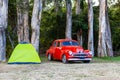 Red vintage car parked near small green tent.