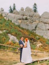 Beautiful redhair bride with groom posing on background of green forest mountains. Royalty Free Stock Photo