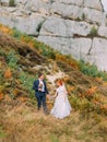 Beautiful redhair bride with happy groom walking together on background of green forest mountains. Royalty Free Stock Photo