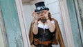 Beautiful redhair steampunk girl with goggles on black hat outside toilet background. Old-fashioned Royalty Free Stock Photo