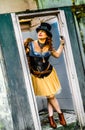 Beautiful redhair steampunk girl with goggles on black hat outside toilet background. Old-fashioned Royalty Free Stock Photo