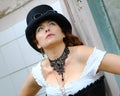 Beautiful redhair steampunk girl with goggles on black hat outside toilet background. Old-fashioned Royalty Free Stock Photo