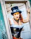 Beautiful redhair steampunk girl with goggles on black hat outside toilet background. Old-fashioned Royalty Free Stock Photo