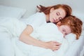 Beautiful redhaired ginger woman hugging asleep her daughter under white blanket at cozy morning home.corona infection Royalty Free Stock Photo