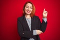 Beautiful redhead business woman wearing elegant jacket over isolated red background with a big smile on face, pointing with hand Royalty Free Stock Photo