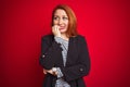 Beautiful redhead business woman wearing elegant jacket over isolated red background looking stressed and nervous with hands on Royalty Free Stock Photo