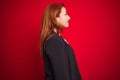 Beautiful redhead business woman wearing elegant jacket over isolated red background looking to side, relax profile pose with Royalty Free Stock Photo