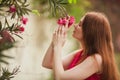 Beautiful redhead girl inhales the aroma of the flower. Red flower growing on a tree. Royalty Free Stock Photo