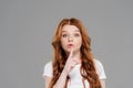 Beautiful redhead girl looking at camera and doing silent gesture isolated on grey.