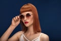 Beautiful redhead girl in sunglasses on blue background. Royalty Free Stock Photo