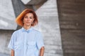 Beautiful redhead girl wearing in a striped shirt posing against background of concrete wall. Royalty Free Stock Photo