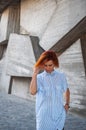 Beautiful redhead girl wearing in a striped shirt posing against background of concrete wall. Royalty Free Stock Photo