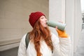Beautiful redhead woman drinking hot tea or coffee from thermos, female tourist enjoys warm drink, rests during her Royalty Free Stock Photo
