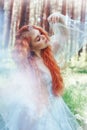 Beautiful redhead woman forest nymph in a blue transparent light dress in the woods spinning in dance. Red hair girls. Art fashion Royalty Free Stock Photo