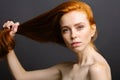 Redhead woman holding her healthy and shiny hair, studio grey Royalty Free Stock Photo