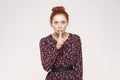 The beautiful redhead woman, holding index finger at lips, raising brows, saying 