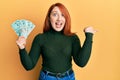 Beautiful redhead woman holding 50 indian rupee banknotes pointing thumb up to the side smiling happy with open mouth Royalty Free Stock Photo