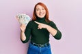 Beautiful redhead woman holding united kingdom pounds smiling happy pointing with hand and finger