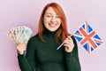 Beautiful redhead woman holding united kingdom pounds and uk flag smiling and laughing hard out loud because funny crazy joke