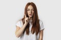 Beautiful redhead woman keeping finger pointed upwards, showing something above her head, making gesture with index finger Royalty Free Stock Photo